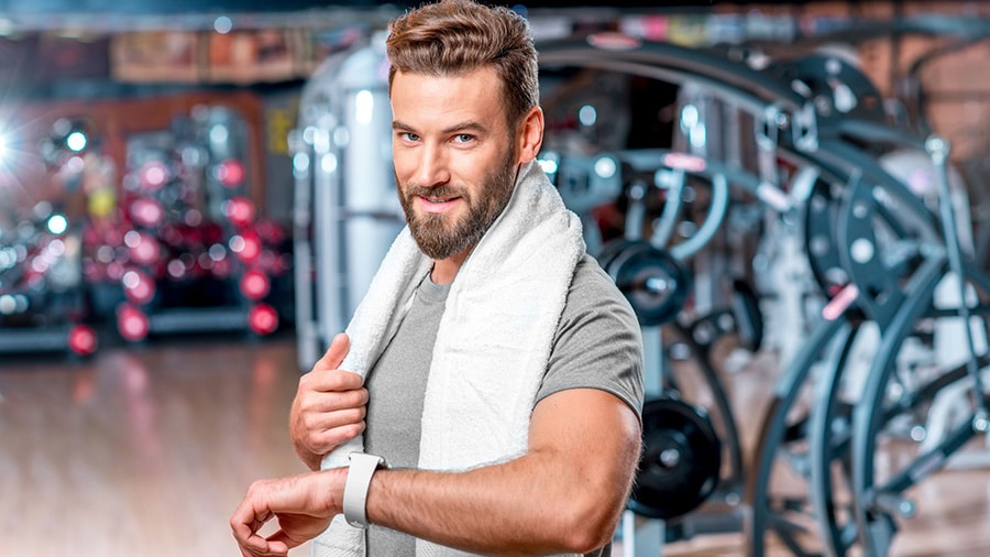 A man in a weight room, towel around his neck, ready to train and keep his sports resolutions.