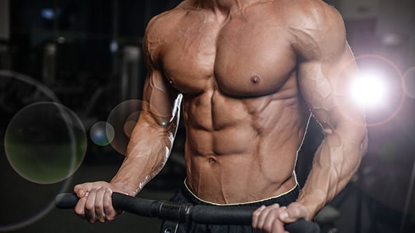 A shirtless man, muscles and abs visible, performs a biceps exercise in a gym.