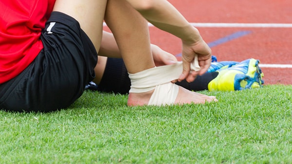 A child sitting on gauze bandages his ankle following an injury.