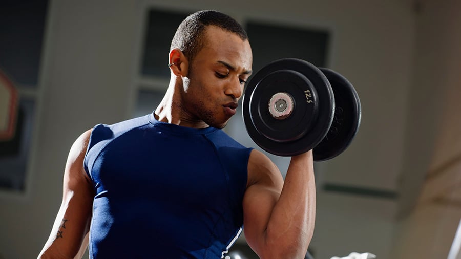 A weightlifter in a blue tank top performs a biceps curl exercise with dumbbells.