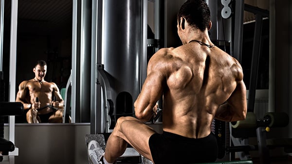 A shirtless man in a weight room performs a horizontal superset back pull.