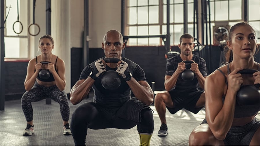 A group of 4 athletes (2 males and 2 females) performs the kettlebell squat exercise as part of an AMRAP training.