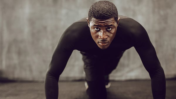 A male athlete in front is in a pump position during a weight training session.