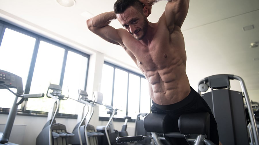 A shirtless athlete does a lumbar exercise on a lumbar bench.