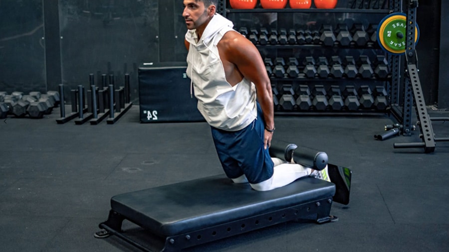 A man in a weight room performs the nordic curl exercise to strengthen his hamstrings.