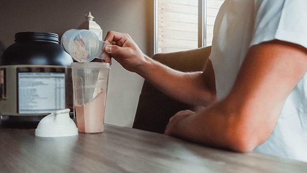 Un homme ajoute de la whey protéine dans un shaker à l'aide d'un doseur.