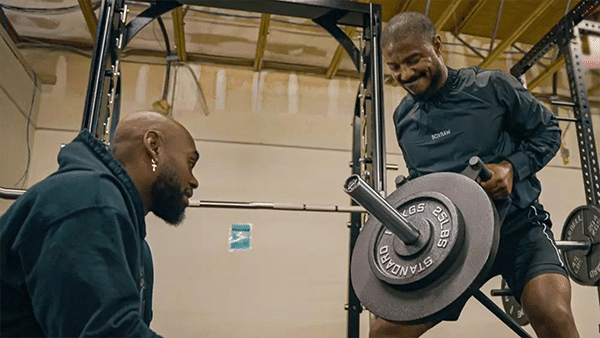 L'entraînement en fitness et en musculation de Michael B. Jordan, qui effectue un exercice de renforcement musculaire avec une barre et des poids en salle de sport, en compagnie de son coach sportif Corey Calliet.