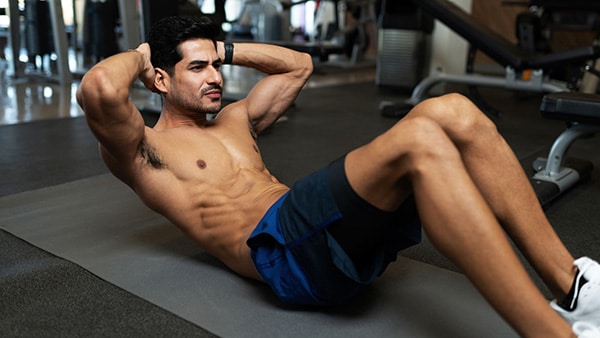 A shirtless man performs the crunch exercise to build up his abs in a fitness and weight room.