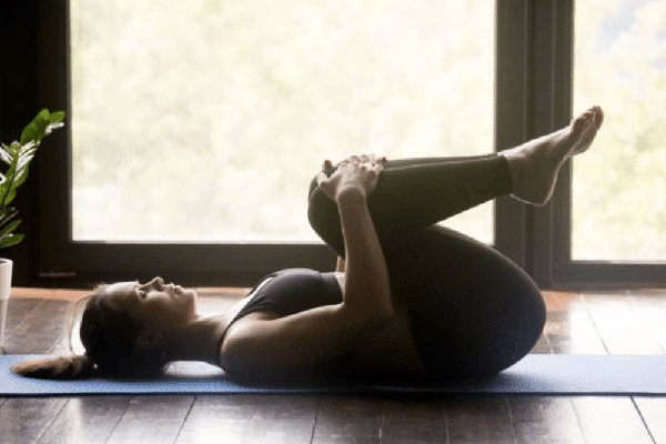 On a fitness mat, a woman performs lumbar stretches.