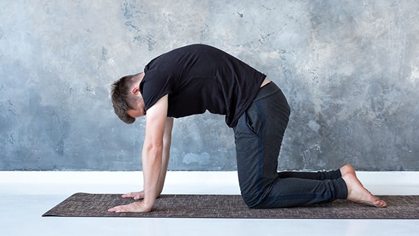 A man on all fours on a yoga mat does the hollow back, round back stretching exercise.