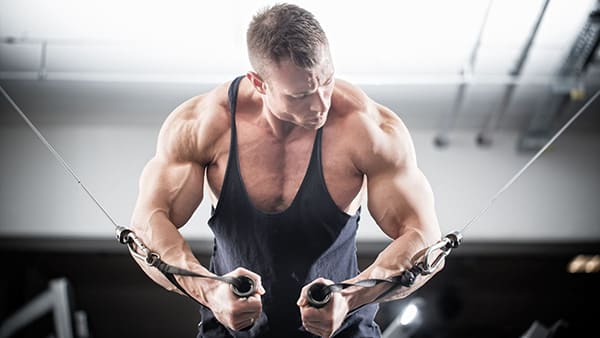 A muscular athlete in a black tank top performs a two-pulley exercise to strengthen his pectoral muscles.