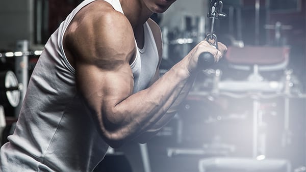 A sportsman in a tank top performs the triceps extension exercise on the high pulley.