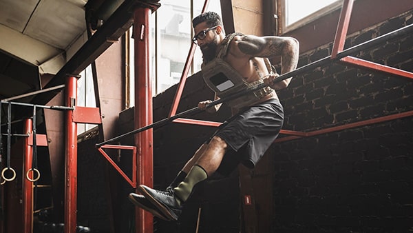 A man wearing a weighted vest performs a muscle-up in a fitness and body-building gym.