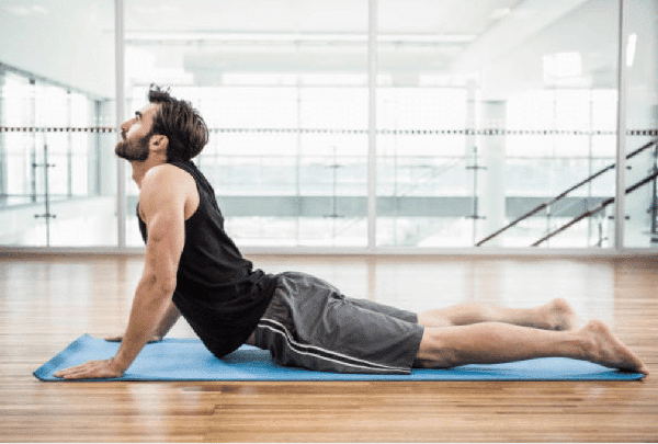 Sur un tapis de sport, un homme en short et en débardeur effectue la posture de yoga du cobra.