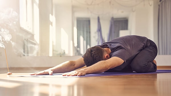 A man on a fitness mat performs the child's pose (or balasana).