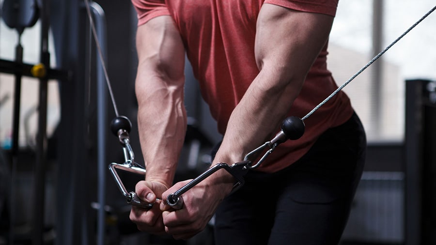 A bodybuilder wearing a red T-shirt performs a pectoral exercise on the opposite pulley.