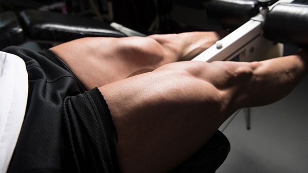 The quadriceps of a man in shorts performing a thigh-building exercise in a gym.