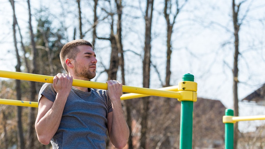 An athletic man pulls on a horizontal bar in a street workout park.