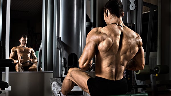 A shirtless man performs a horizontal pulley pull exercise in a fitness center.