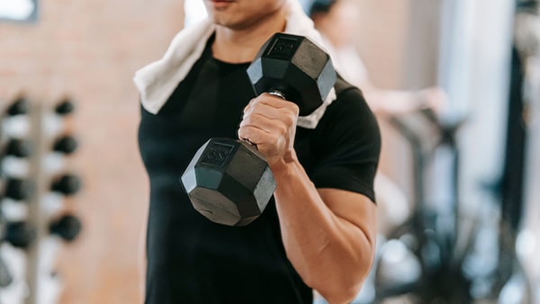 A bodybuilder with a towel around his neck and a dumbbell in his left hand.