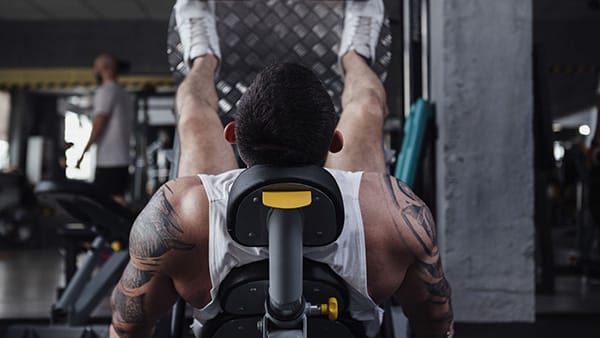 Un homme sportif en débardeur effectue l'exercice de la presse inclinée dans une salle de musculation.