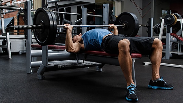 Un homme dans une salle de musculation fait du développé couché sur un banc.