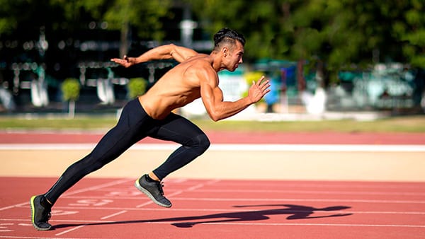 A shirtless man sprints down an athletics track.