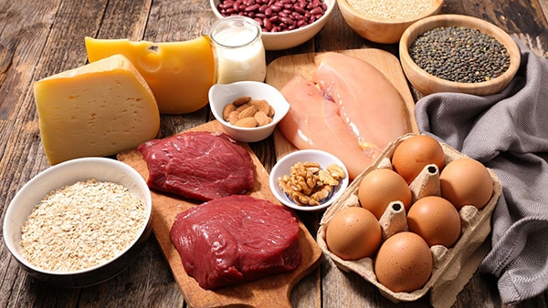 A wooden table with protein-rich foods: beef, chicken, eggs, cheese, almonds, etc.