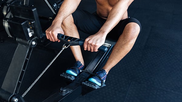 Un homme torse nu fait un échauffement cardio sur un rameur dans une salle de fitness.