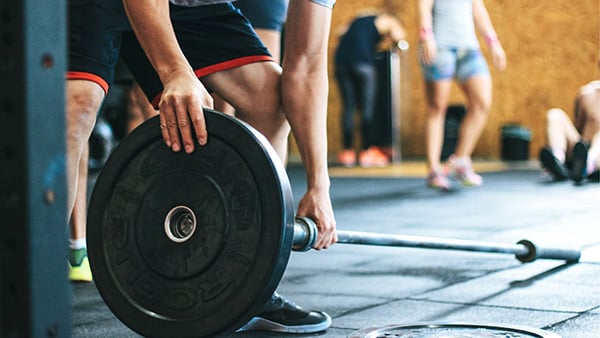 A man in shorts in a fitness center adds a weight disc to a barbell.