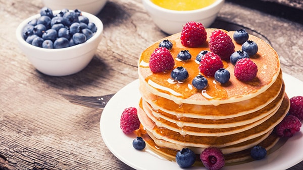 Une assiette remplie de pancakes healthy, parsemés de myrtilles et de framboises.