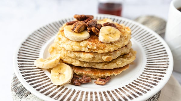 Une assiette avec 4 pancakes protéinés, agrémentés de banane et d'oléagineux.