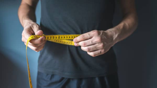 A man measures his belly circumference with a tape measure to monitor the effectiveness of his body recomposition.