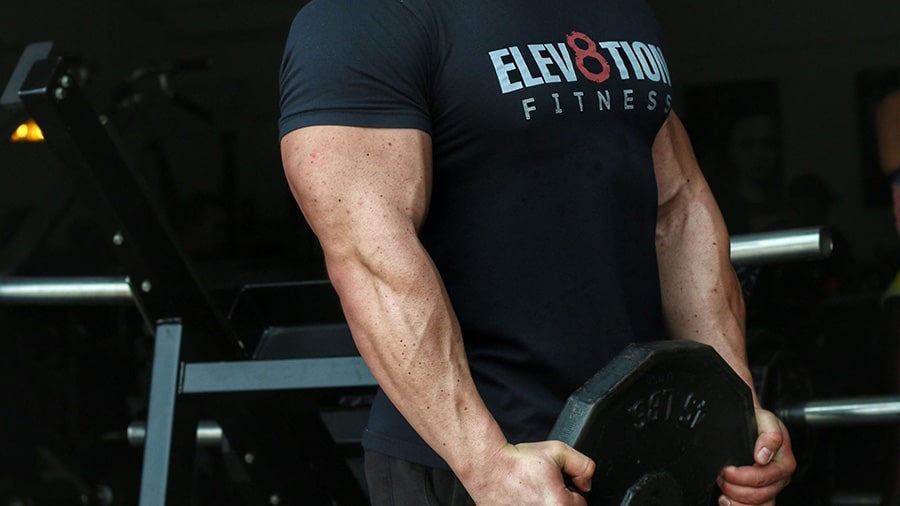 Le coach sportif Julien Quaglierini en t-shirt en train de porter un disque de poids, les biceps et les triceps congestionnés.