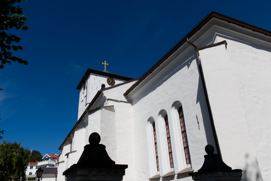 kyrka fotad i skarp vinkel nerifrån, blå himmel och en staty som ser kolsvart ut i kontrasten mot det starka ljuset