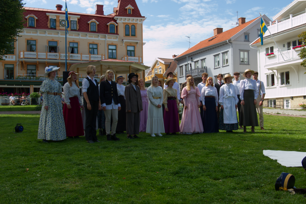 Ett stort gäng, varierande åldrar, uppställda för fotografering i vackra kläder på gräsmatta framför grand hotel Marstrand