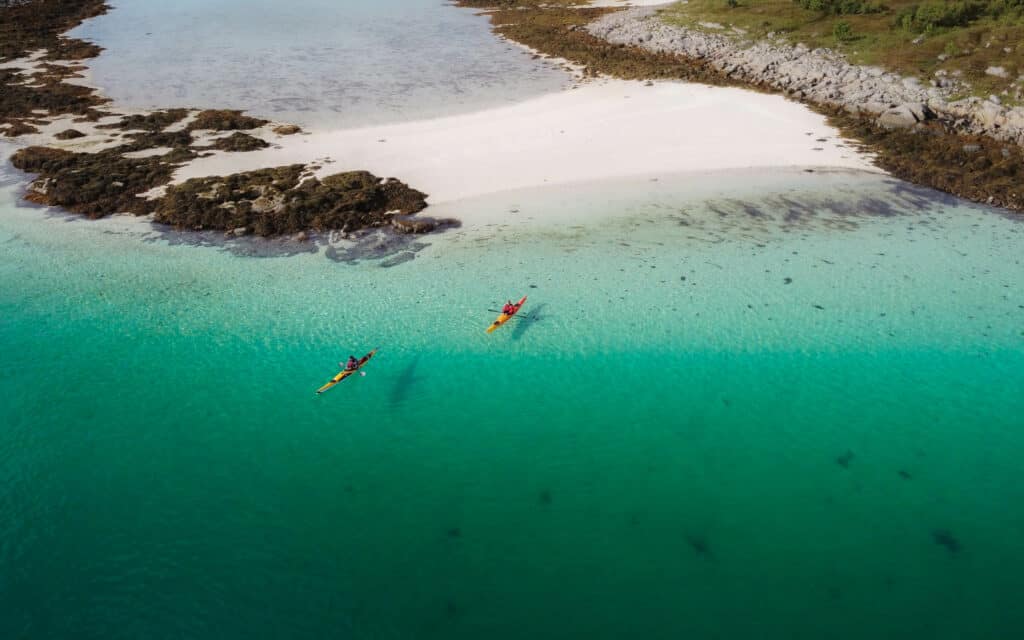 2 sea kayakers in crystal blue water and sand beach on an island in Bergsfjord senja