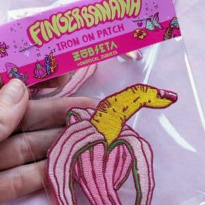 Quirky iron-on patch titled 'Finger Banana' featuring a playful, sexy and surreal design of a peeled banana with a finger. The patch is intricately embroidered with yellow and pink threads, creating a vibrant and eye-catching effect. this patch adds a unique and humorous touch to jackets, bags, or hats