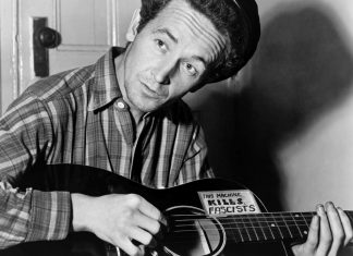 Woody Guthrie playing a guitar that has a sticker attached reading: This Machine Kills Fascists. Photo: Taken 8 March 1943 by Al Aumuller. Collection: New York World-Telegram and the Sun, Library of Congress. Public Domain.
