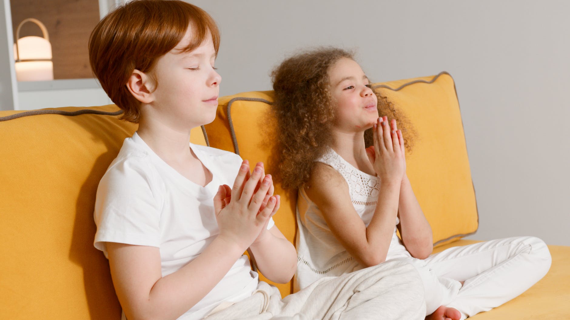 photo of two kids doing yoga on an orange sofa