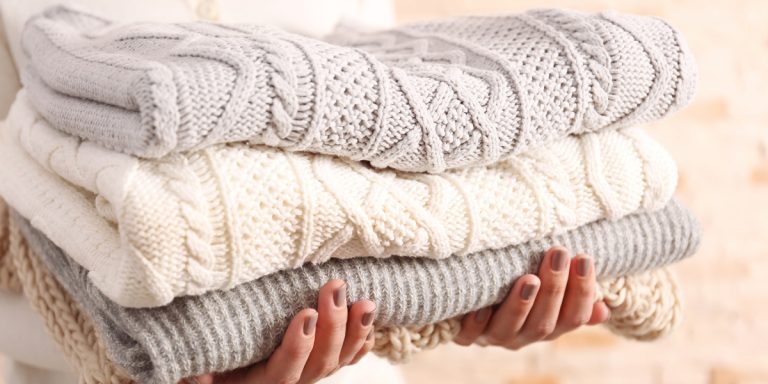 a girl holding a pile of chunky knit jumpers