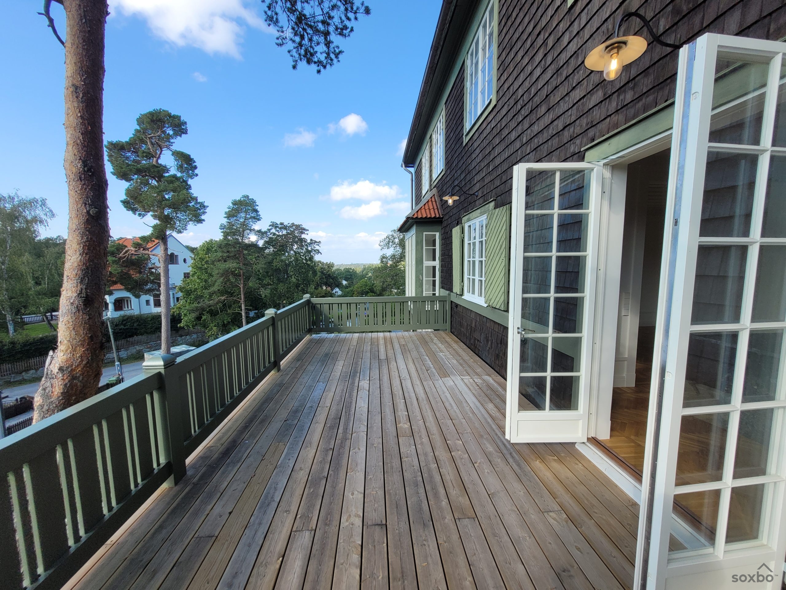 Stor veranda i anslutning till sekelskiftesvillan Villa Tallbo på Lidingö med plats för loungemöbler och utsikt över grönskande omgivningar.