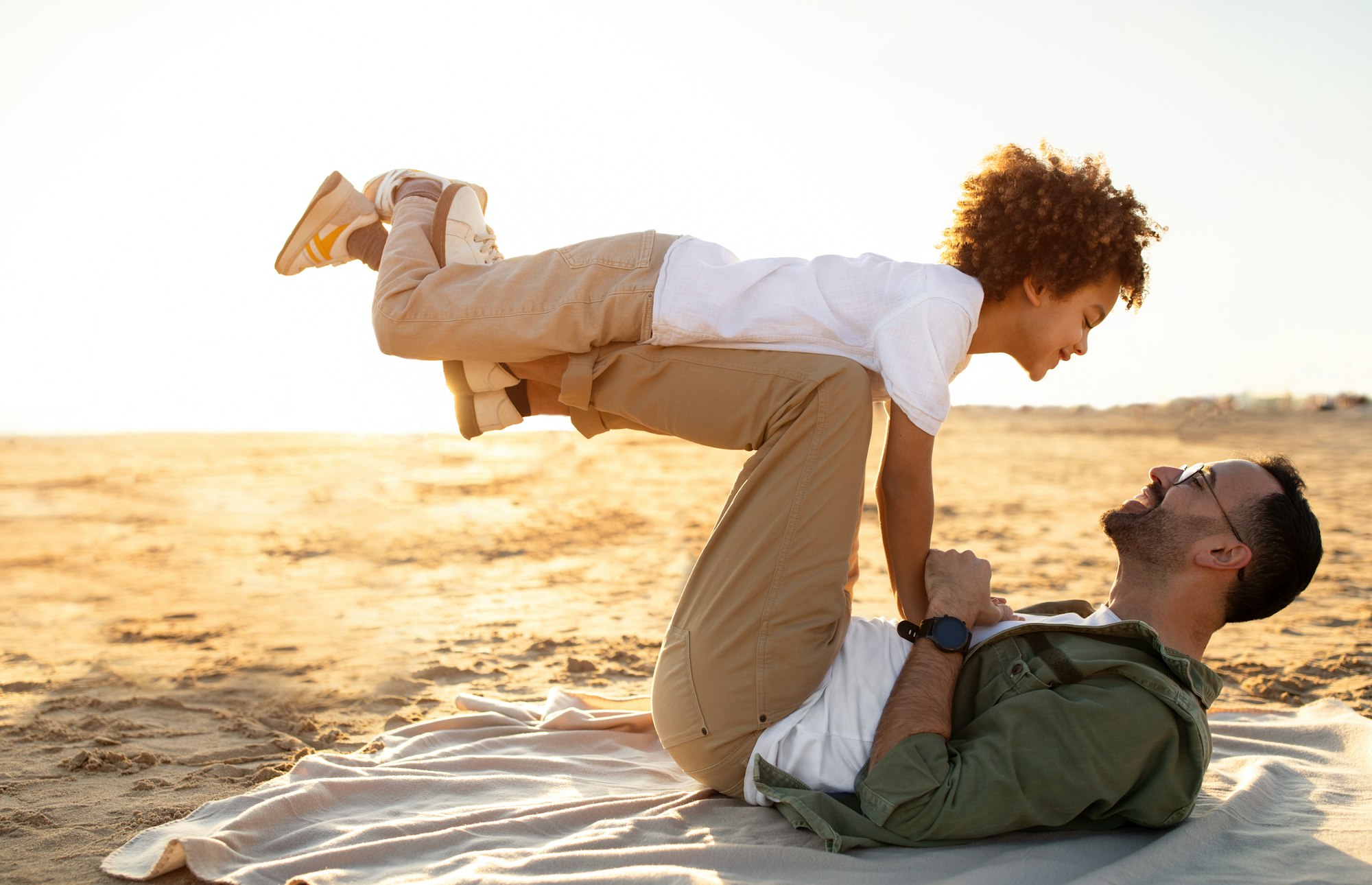 Young father and his son sharing a special moment on the coastline, man lying on plaid and raising