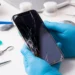 Tekniker med blå handskar håller en iPhone 13 med spräckt skärm redo för reparation – laga iPhone 13