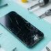 Teknikera med blå handskar håller en iPhone 14 med spräckt skärm redo för reparation – laga iPhone 14