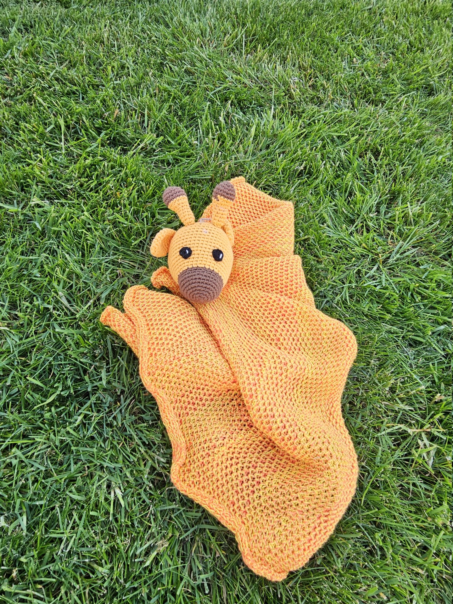 Håndhæklet sikkerhedstæppe med girafmotiv, orange og gult, på græs. Danskproduceret.