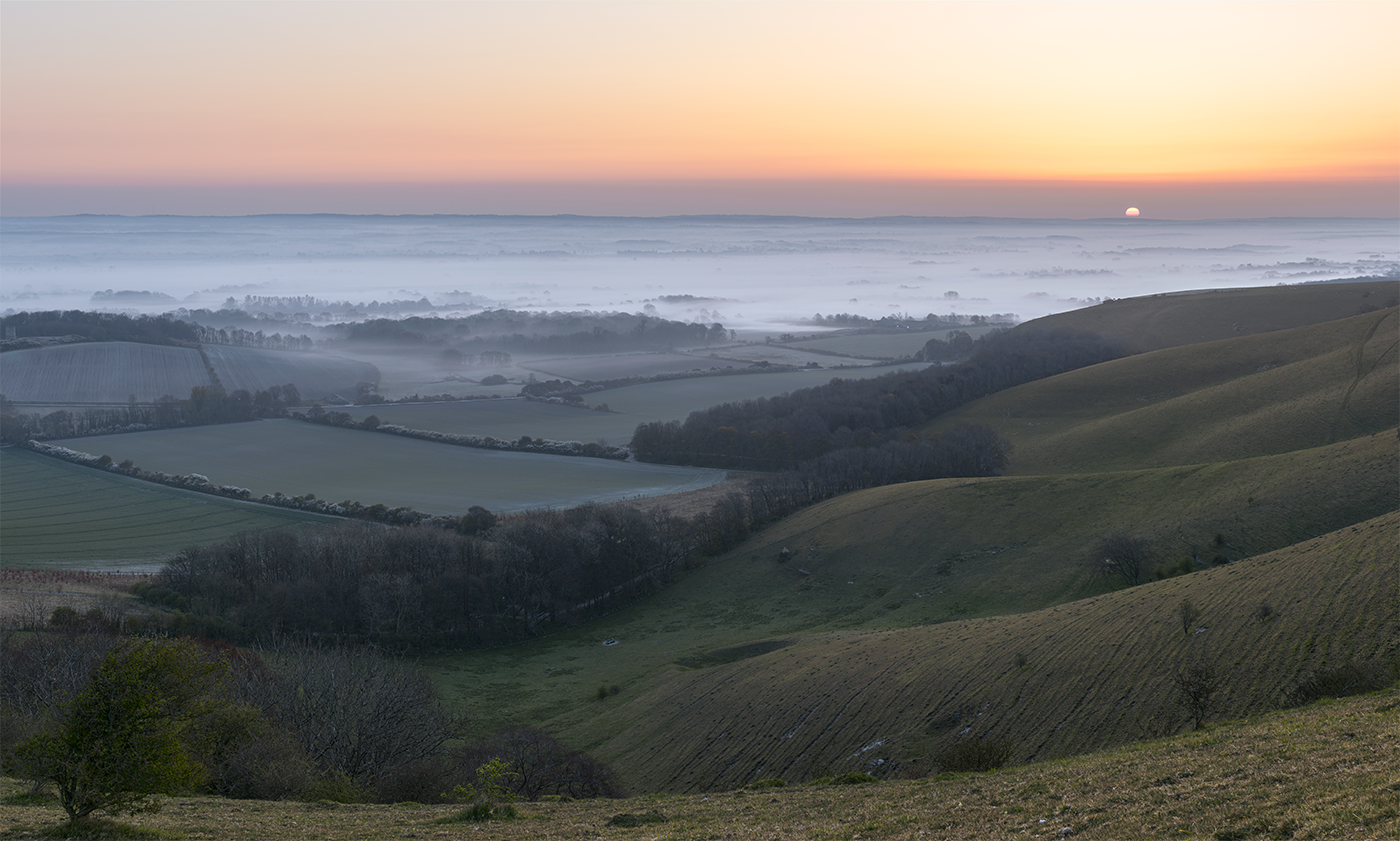 The sun rises over an early morning mist inversion at the foot of the South Downs.