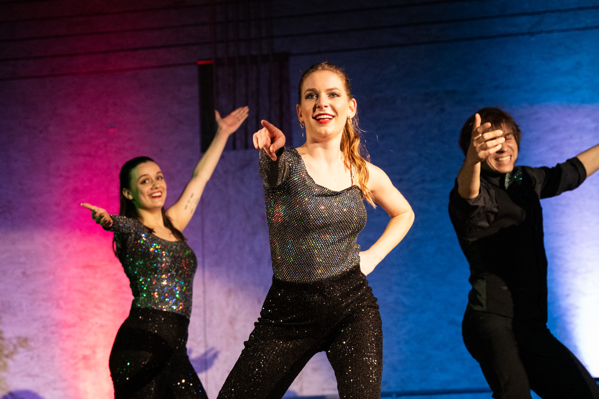 Drei Showact-Performer in glitzernden Outfits tanzen auf der Bühne mit blauer und pinker Bühnenbeleuchtung – Showact buchen Schweiz