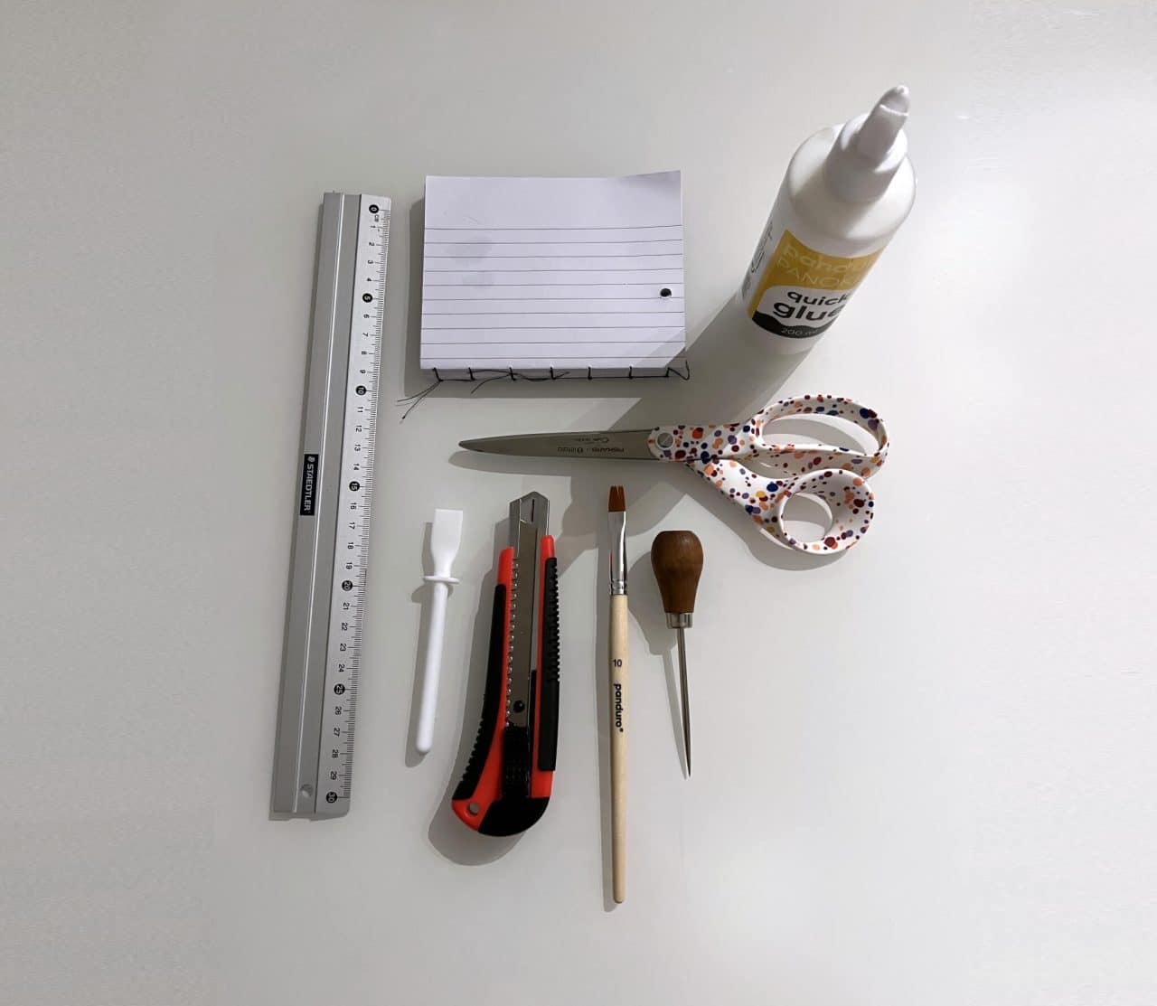 Linjal, saks, lim og diverse verktøy ligger på et bord