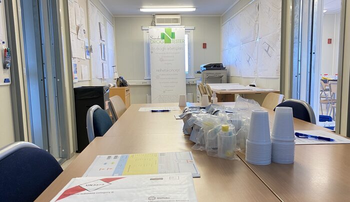 Ett konferensrum där en rollup med svenska drogtesters logotyp syns, samt ett bord där utrustning för drogtestning finns.